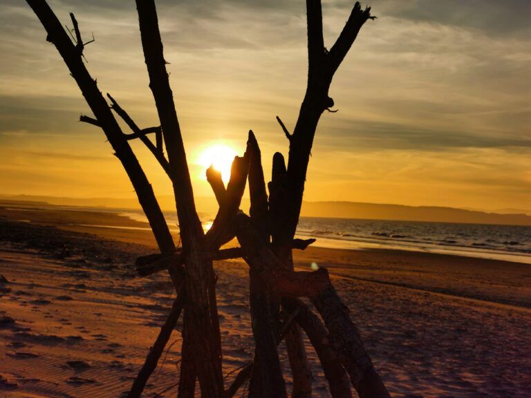 a wigwam of sticks against a sunset sky in a beach setting